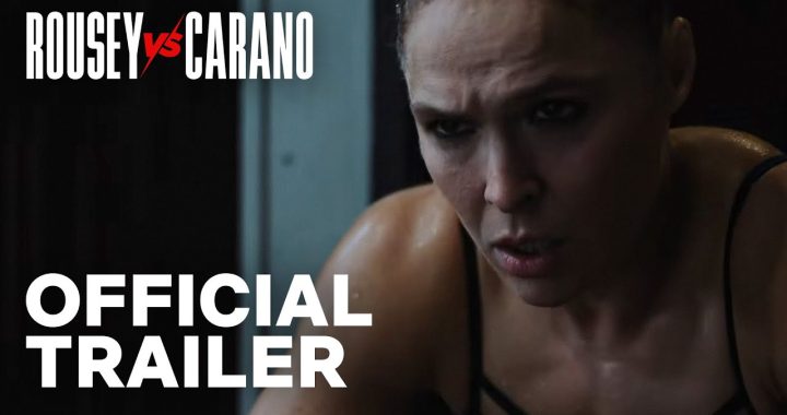 Official trailer thumbnail: close-up of a focused female fighter with sweat, overlaid with 'ROUSEY vs CARANO' and 'OFFICIAL TRAILER'.