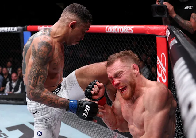 Two UFC fighters in the octagon: one lands a knee to the other's face, both battered and bleeding, with a camera crew and spectators in the background.