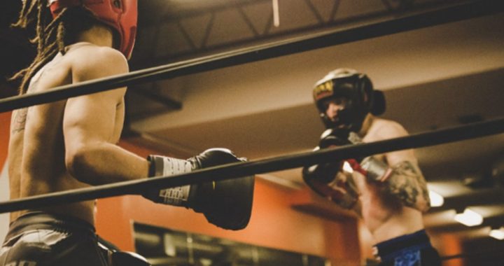 Two boxers spar in a gym ring; one in red headgear, the other in blue shorts and black gloves._Turns into a concise description of action and context.