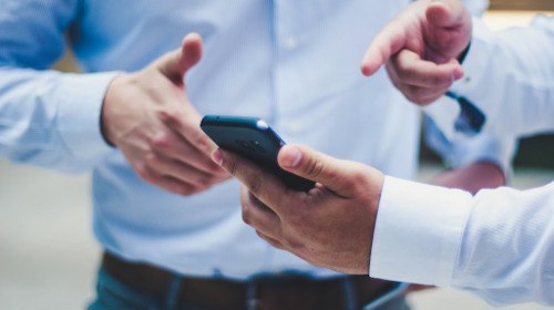 Two people in collared shirts exchange a smartphone during a discussion, focusing on the hands and device between them.