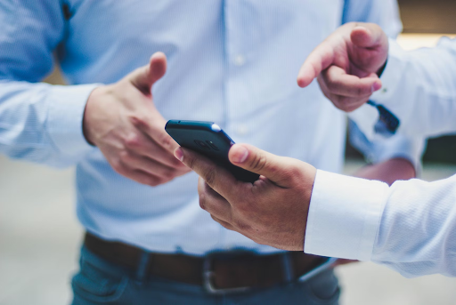 Two people in collared shirts exchange a smartphone during a discussion, focusing on the hands and device between them.