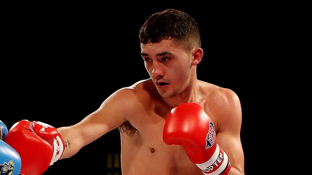 Male boxer throwing a punch with red gloves against a dark background.