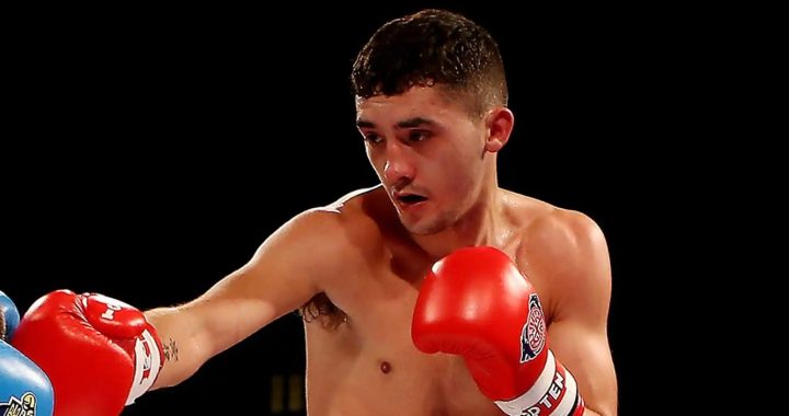 Male boxer throwing a punch with red gloves against a dark background.