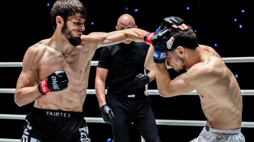 Two shirtless fighters exchange punches in a ring while a referee watches in the background.
