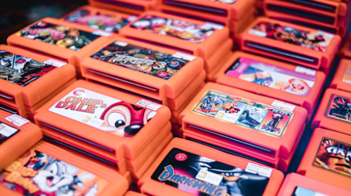 Close-up of stacked orange video game cartridges with colorful labels (e.g., Chip 'n Dale, Darkwing Duck) arranged in a display.