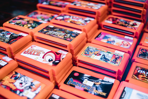 Close-up of stacked orange video game cartridges with colorful labels (e.g., Chip 'n Dale, Darkwing Duck) arranged in a display.