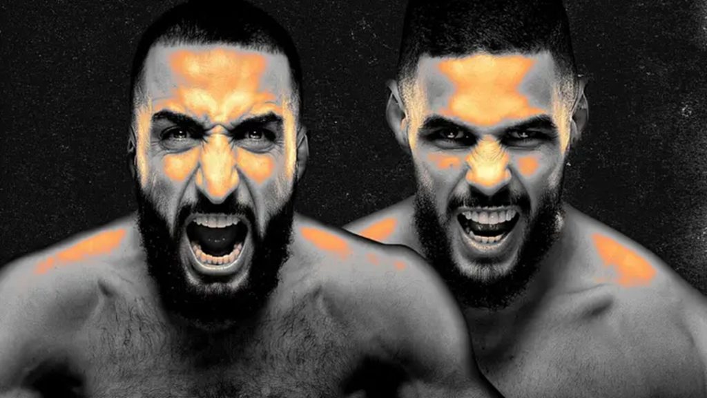 Two shirtless men with beards yell directly at the camera, orange highlights on their faces and shoulders against a dark background.