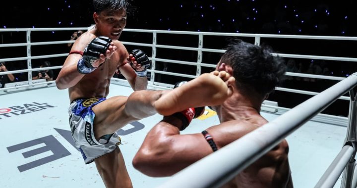 Two male mixed martial arts fighters in a ring; the left fighter delivers a kick as the opponent guards with raised arms.
